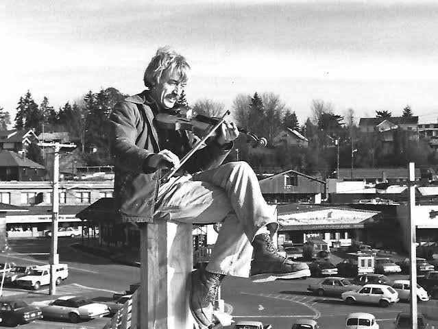 Bill Austin playing violin atop a post overlooking Poulsbo